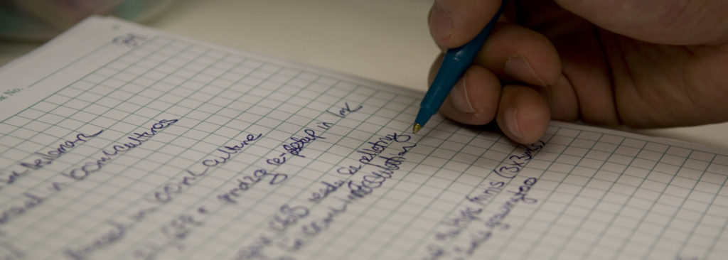 Close up of a hand writing in a lab notebook