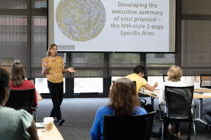 Speaker giving a presentation with a projected slide behind her